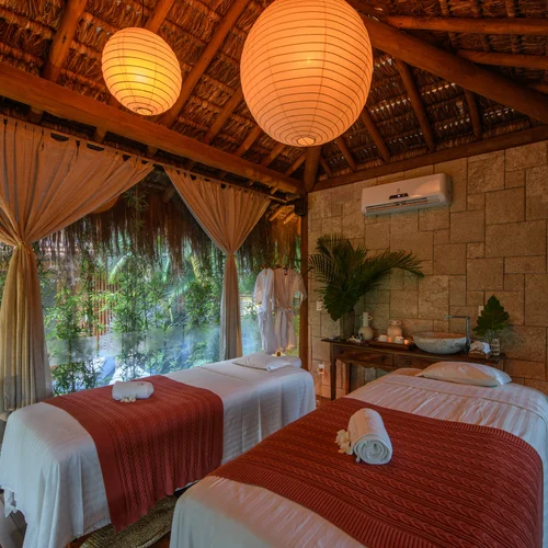 Duas macas de massagem com mantas terracota em cabana de palha cercada pela natureza
